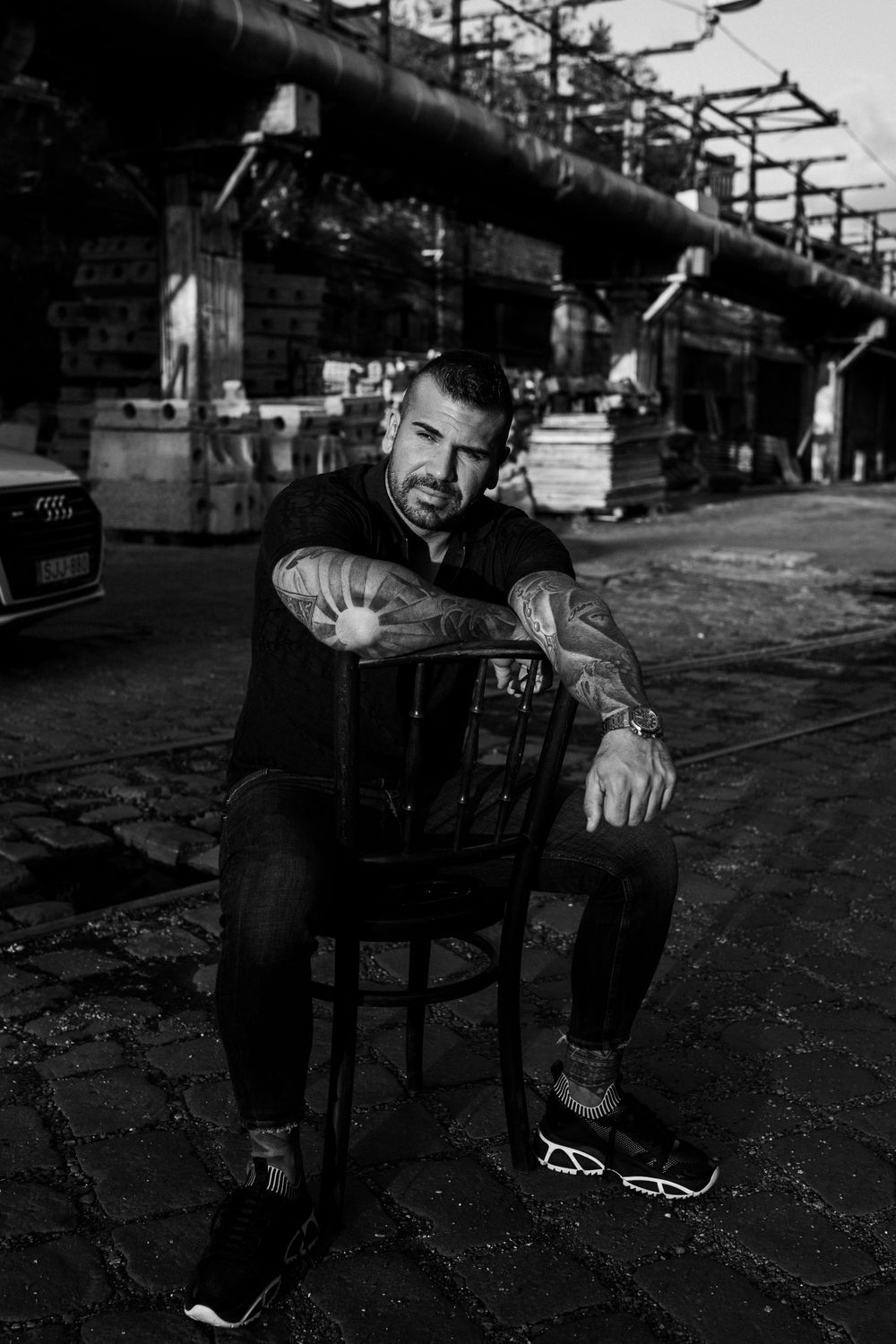 Black and white urban portrait with industrial piping and architecture in background.