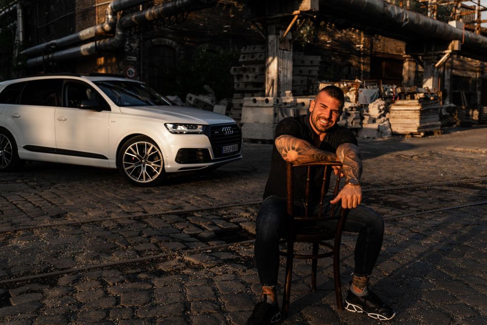 White luxury SUV parked on cobblestone street at sunset with moody urban industrial backdrop.