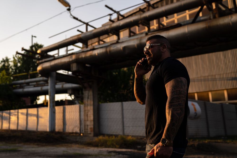 Person in black shirt standing against industrial building during golden hour.