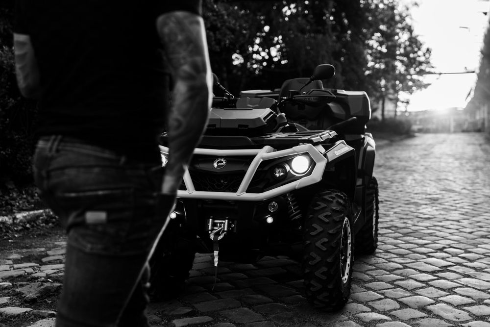 Black ATV on cobblestone street with industrial architecture in background.