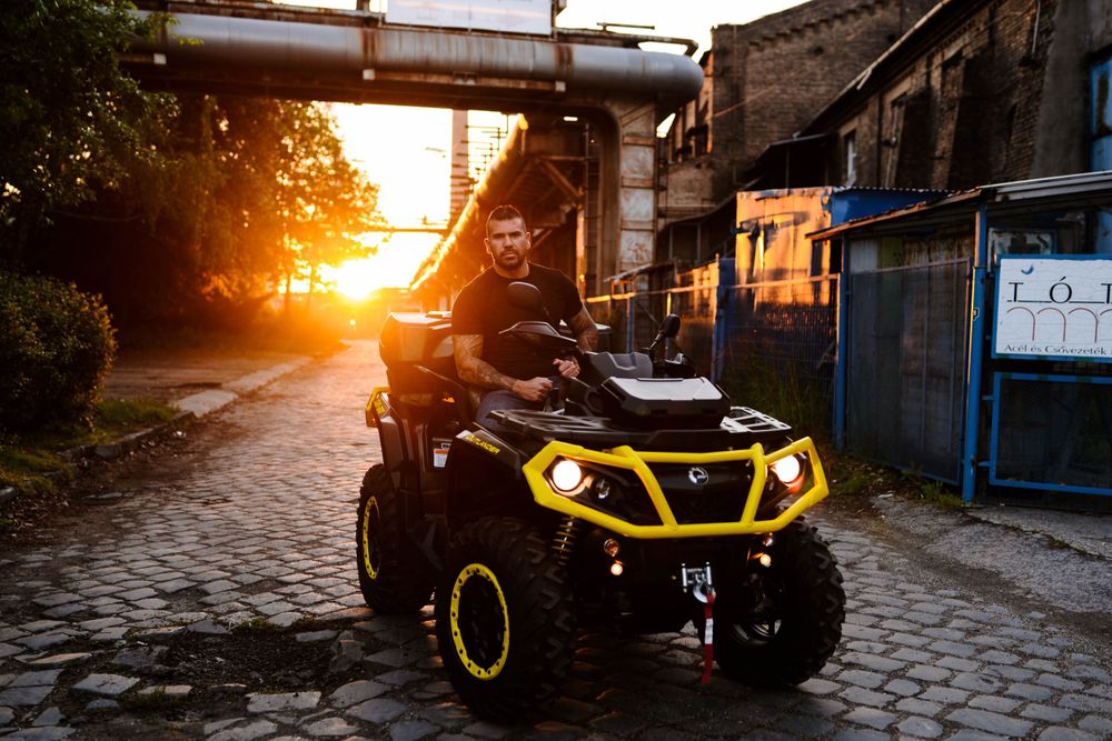 Yellow ATV illuminated at sunset against industrial backdrop with golden lighting.