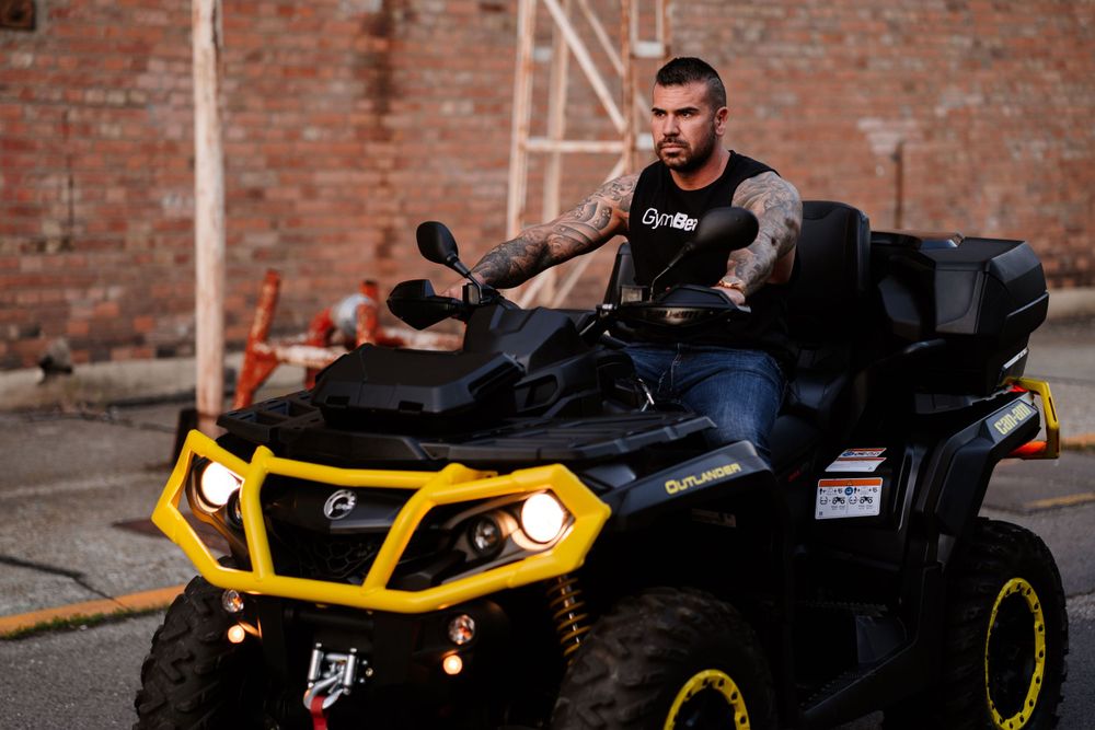 Black and yellow Can-Am ATV parked in front of a rustic brick wall with headlights illuminated.