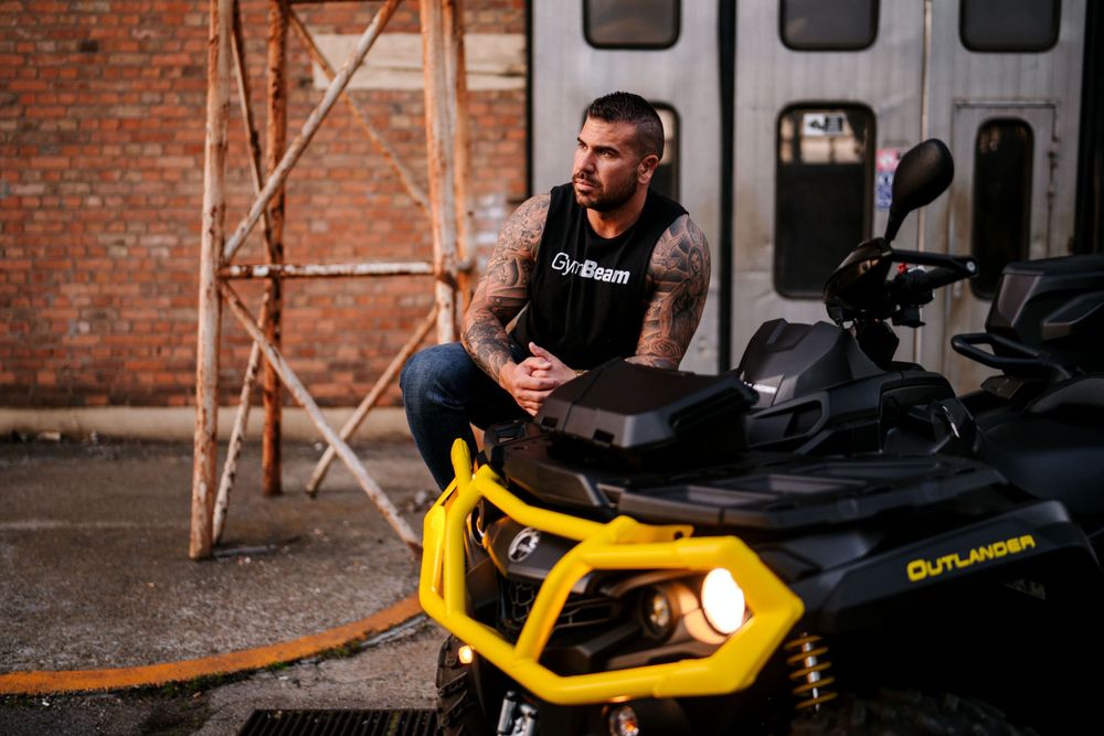 Athletic figure sits on a black and yellow Can-Am ATV in an industrial setting.
