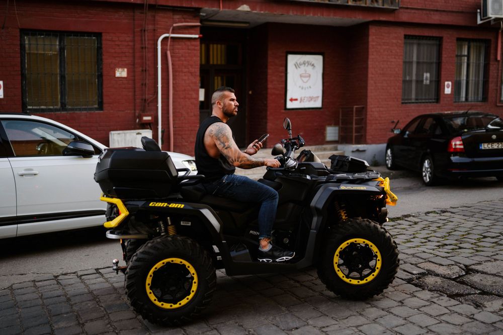 Black ATV with yellow accents cruising on cobblestone street in urban setting.