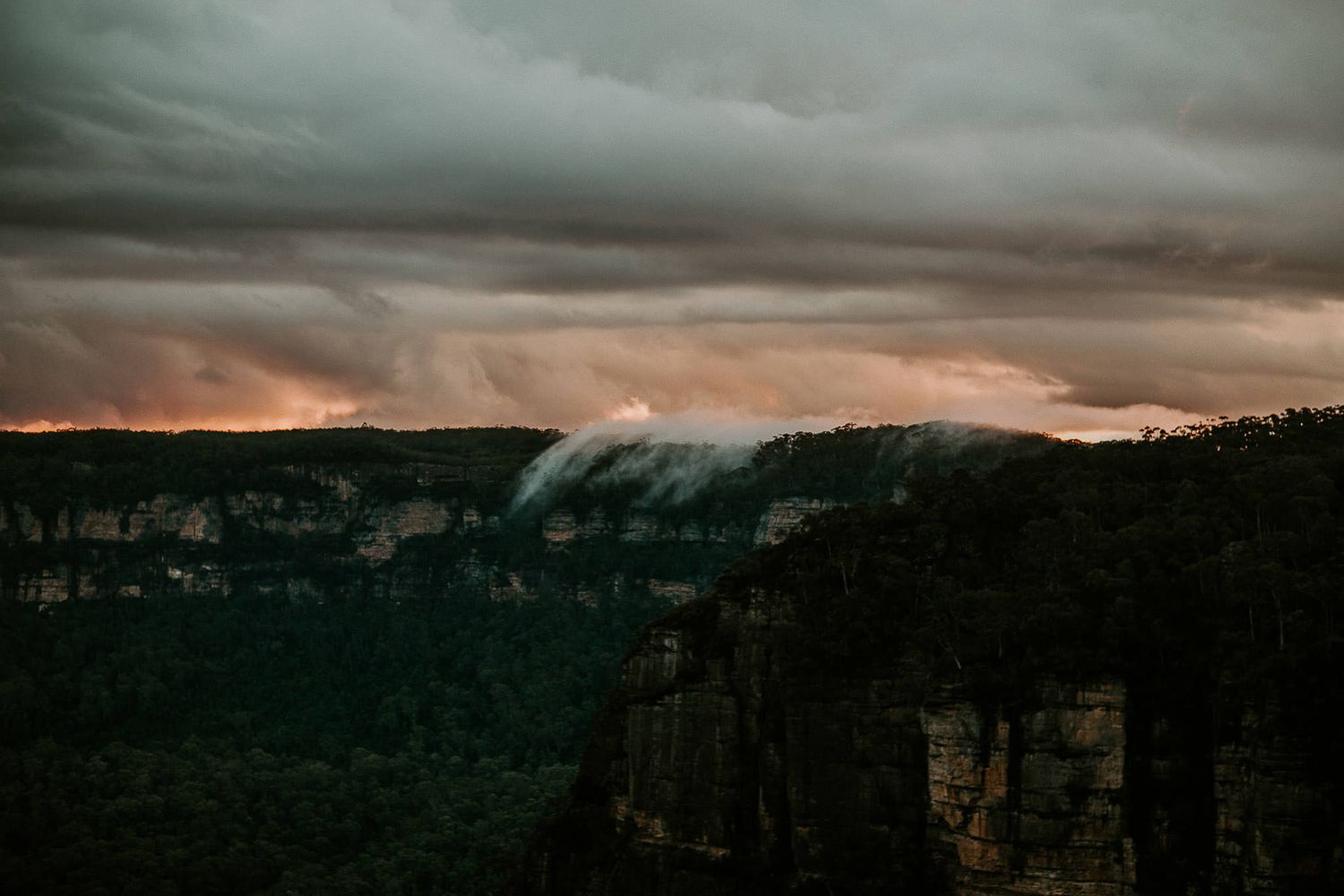 Dramatic sunset sky over mountain cliffs with moody storm clouds.