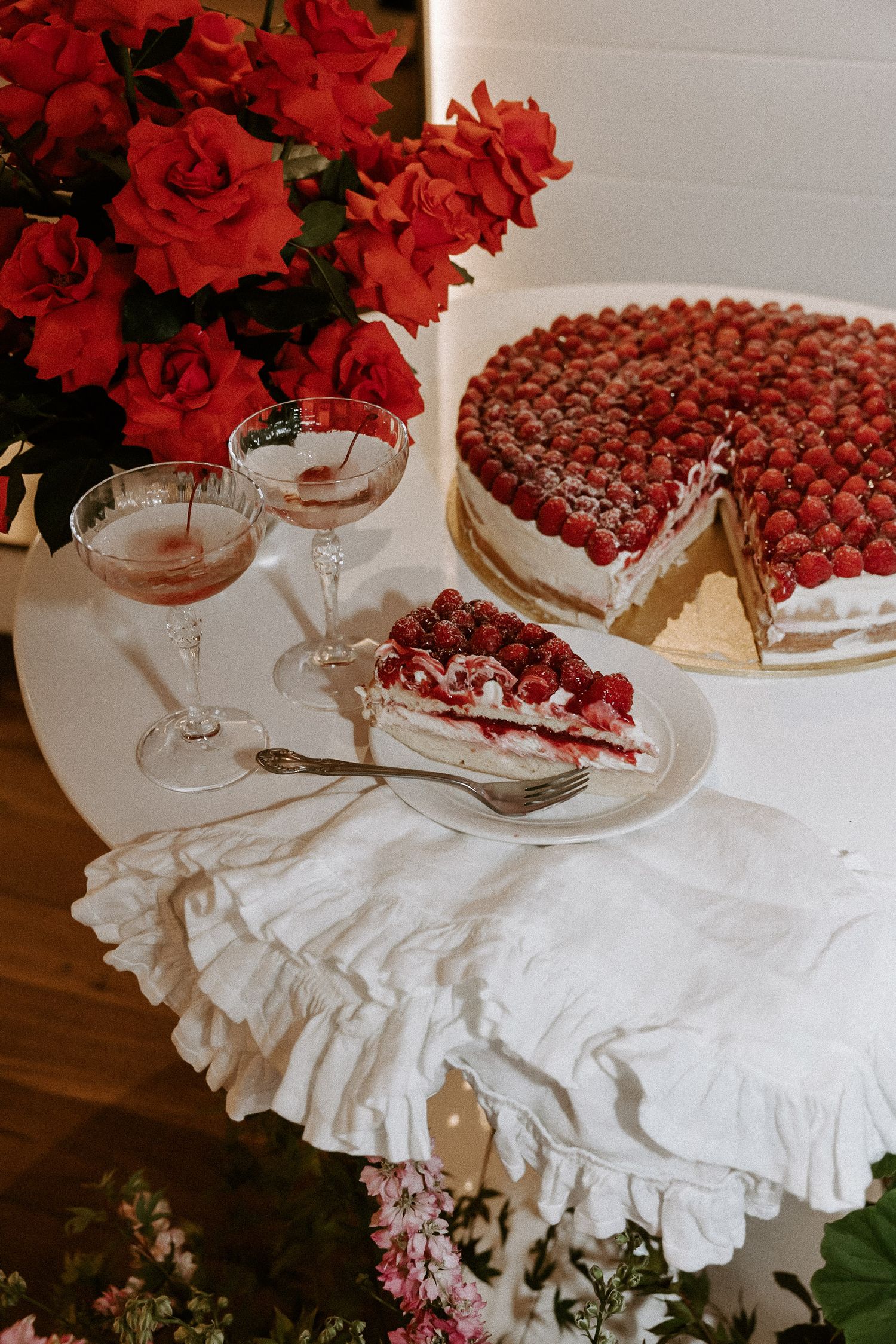 Elegant dessert table with raspberry cake, champagne glasses, and red roses.