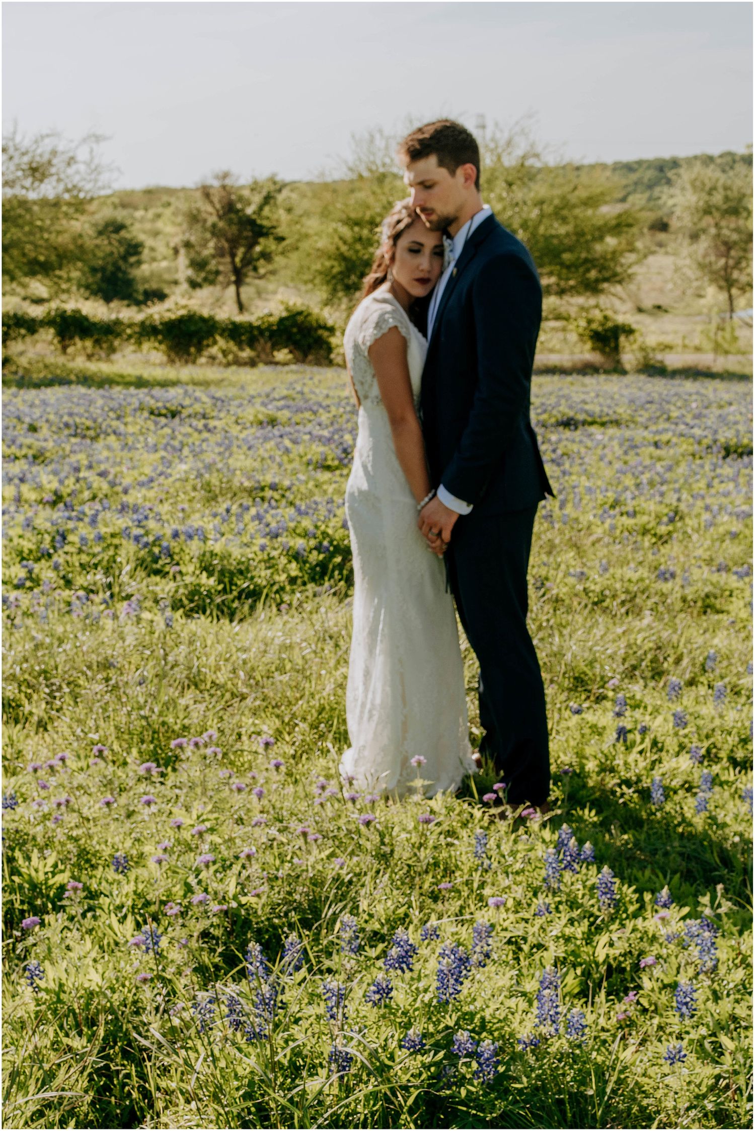 Newlyweds share intimate moment in field of bluebonnets during sunset.