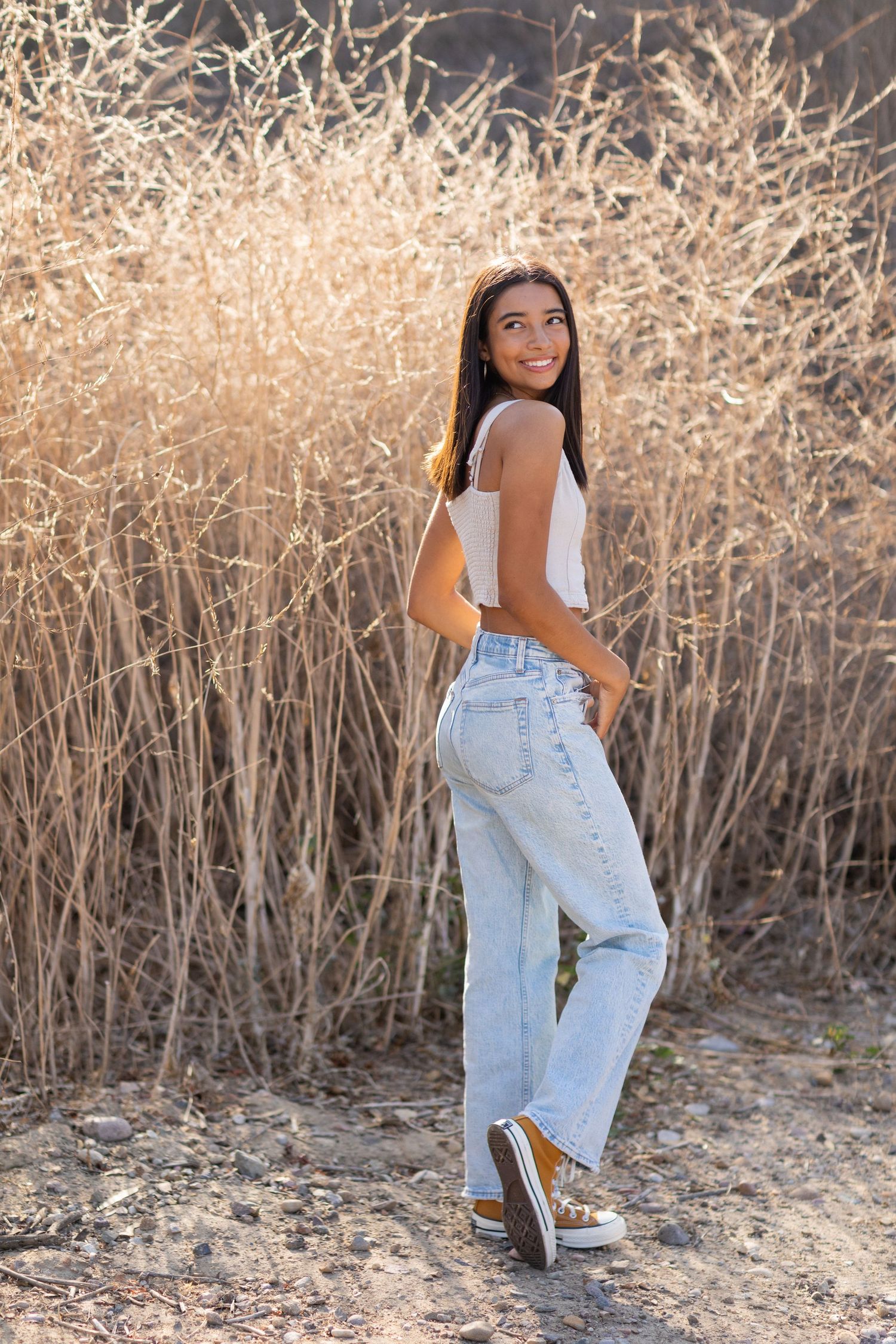 Casual outdoor portrait in jeans and tank top against dried grass background.