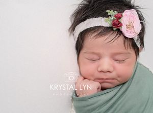 Newborn baby with thick black hair, all wrapped up in sage green