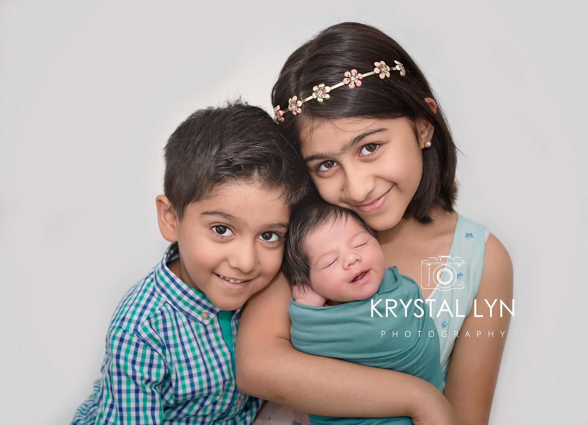 Two older siblings hold their baby sister while Mississauga photographer takes their photo