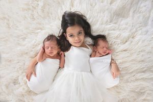 Big sister holding her two new baby sisters for a photo in all white