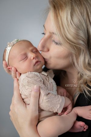 Mommy snuggles her new baby while kissing her tiny cheek