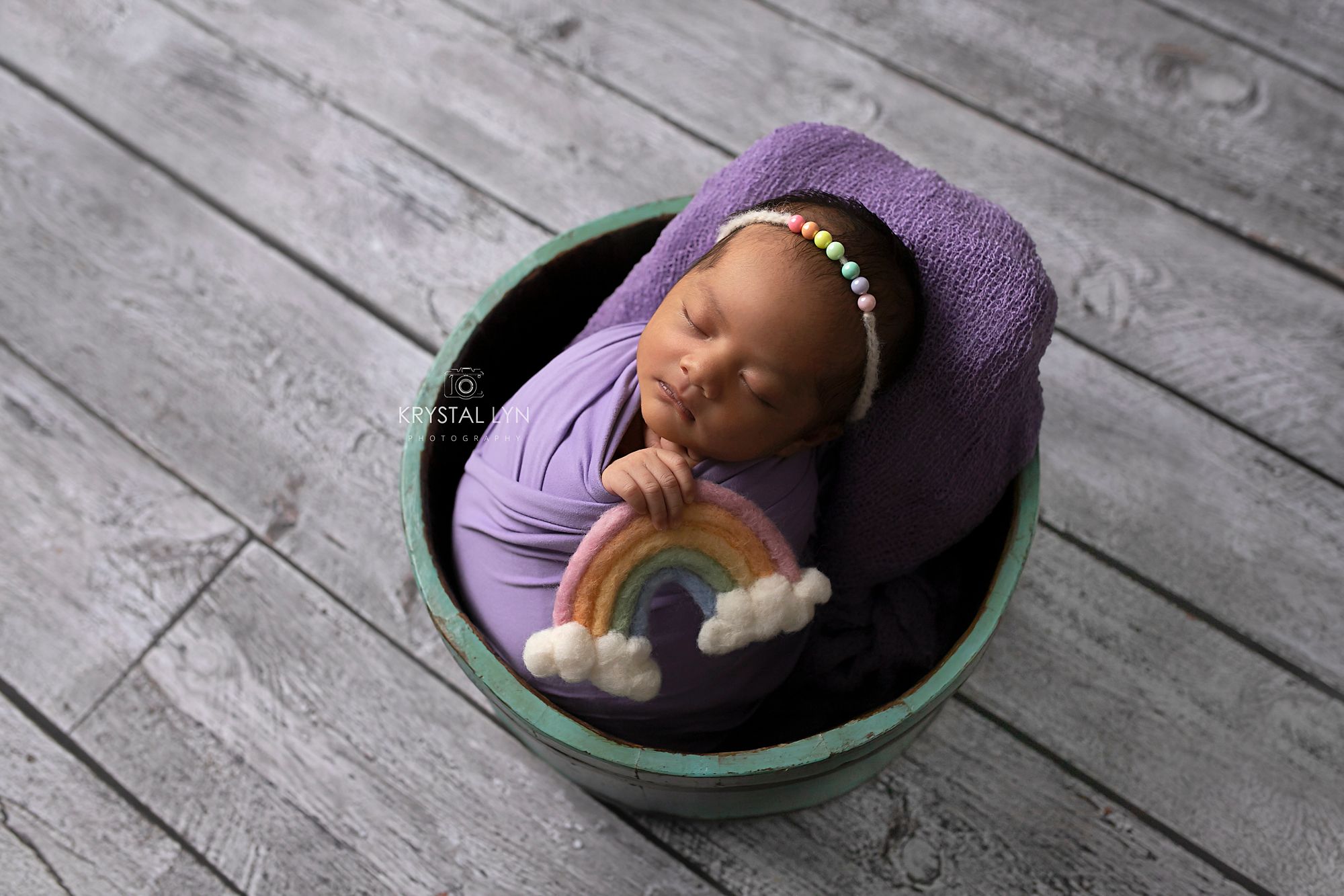 Little one wrapped and posed in a bucket holding a pastel rainbow