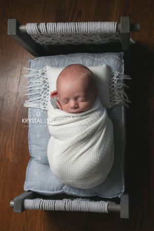 Newborn prop bed in use by this petite baby holding a felted heart