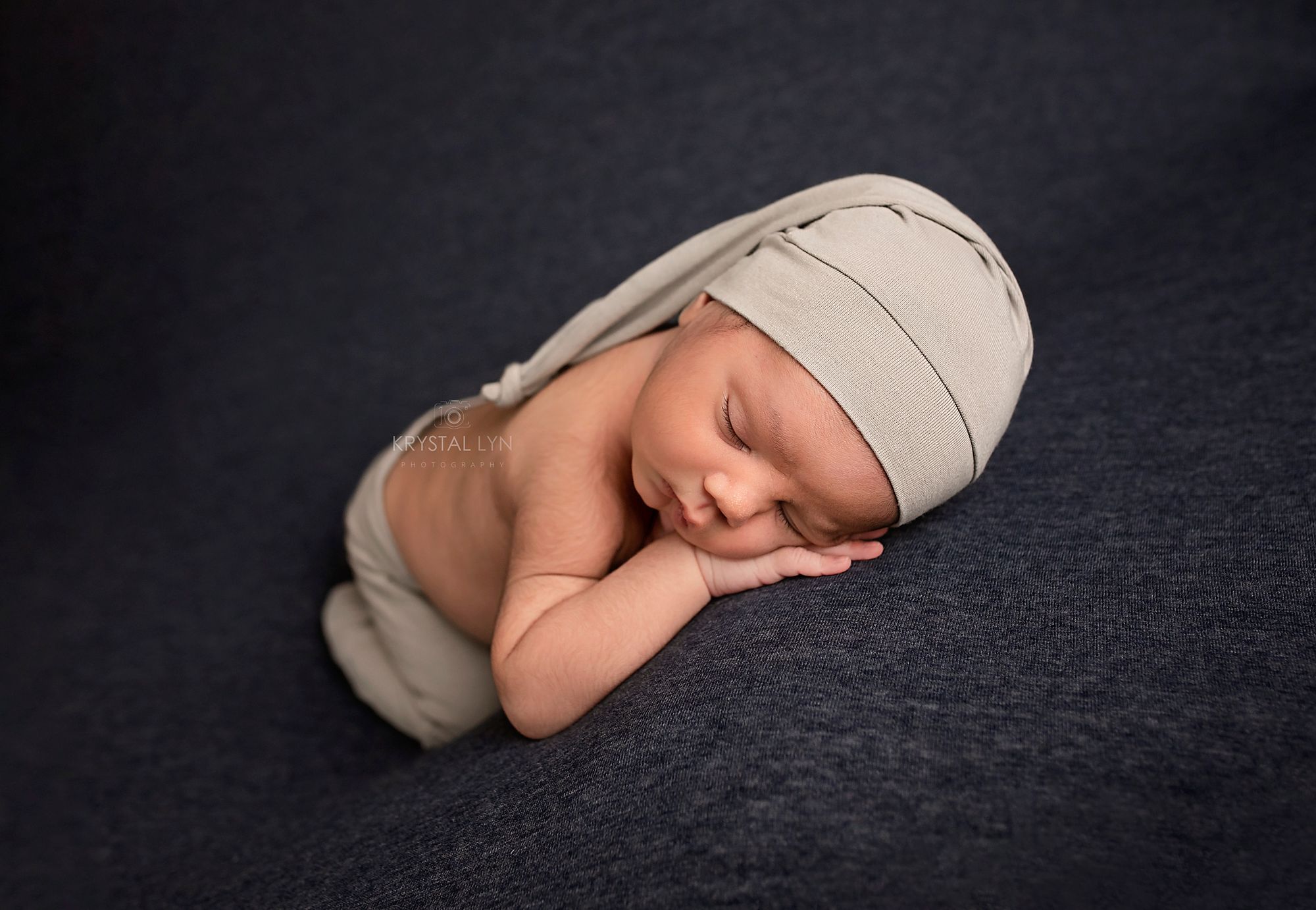 Newborn posed on dark blue wearing grey hat and pants