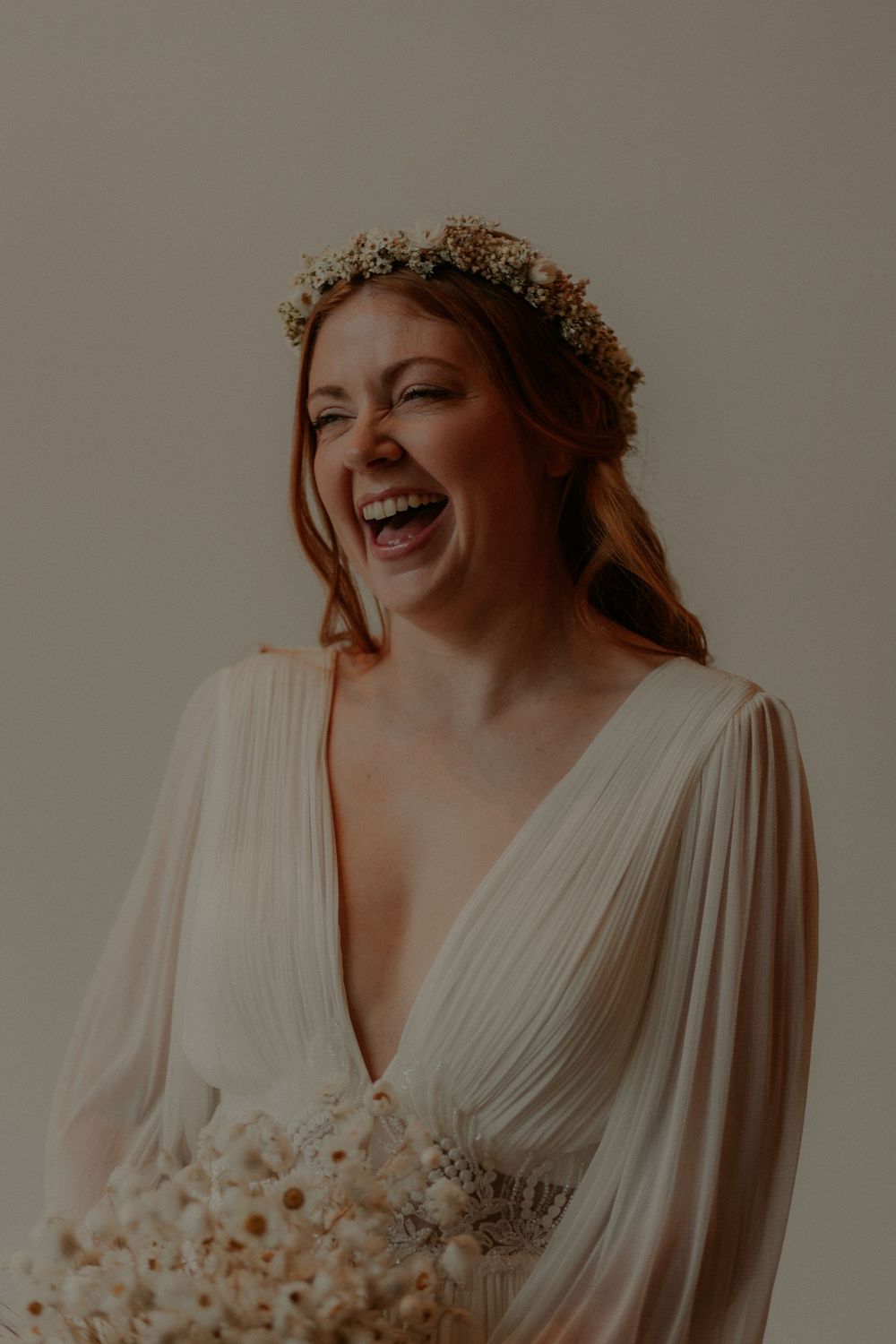 Candid bridal portrait showing genuine laughter while holding dried flower bouquet.