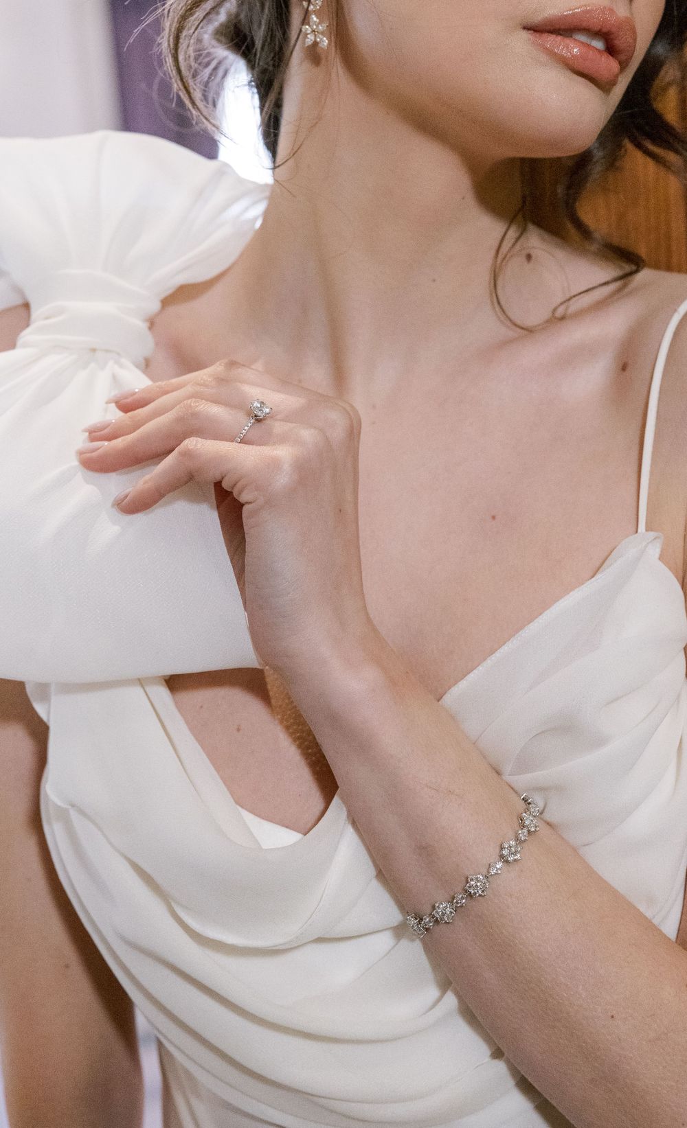 Close-up detail of bride's jewelry and draped white wedding dress fabric.
