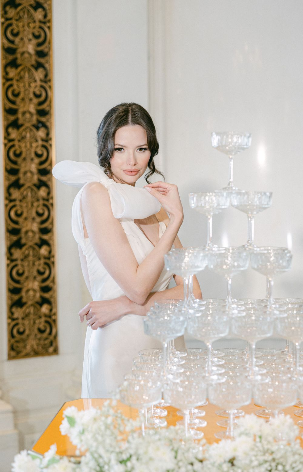 An elegant wedding setting with a champagne tower and floral decorations in a luxurious white room.