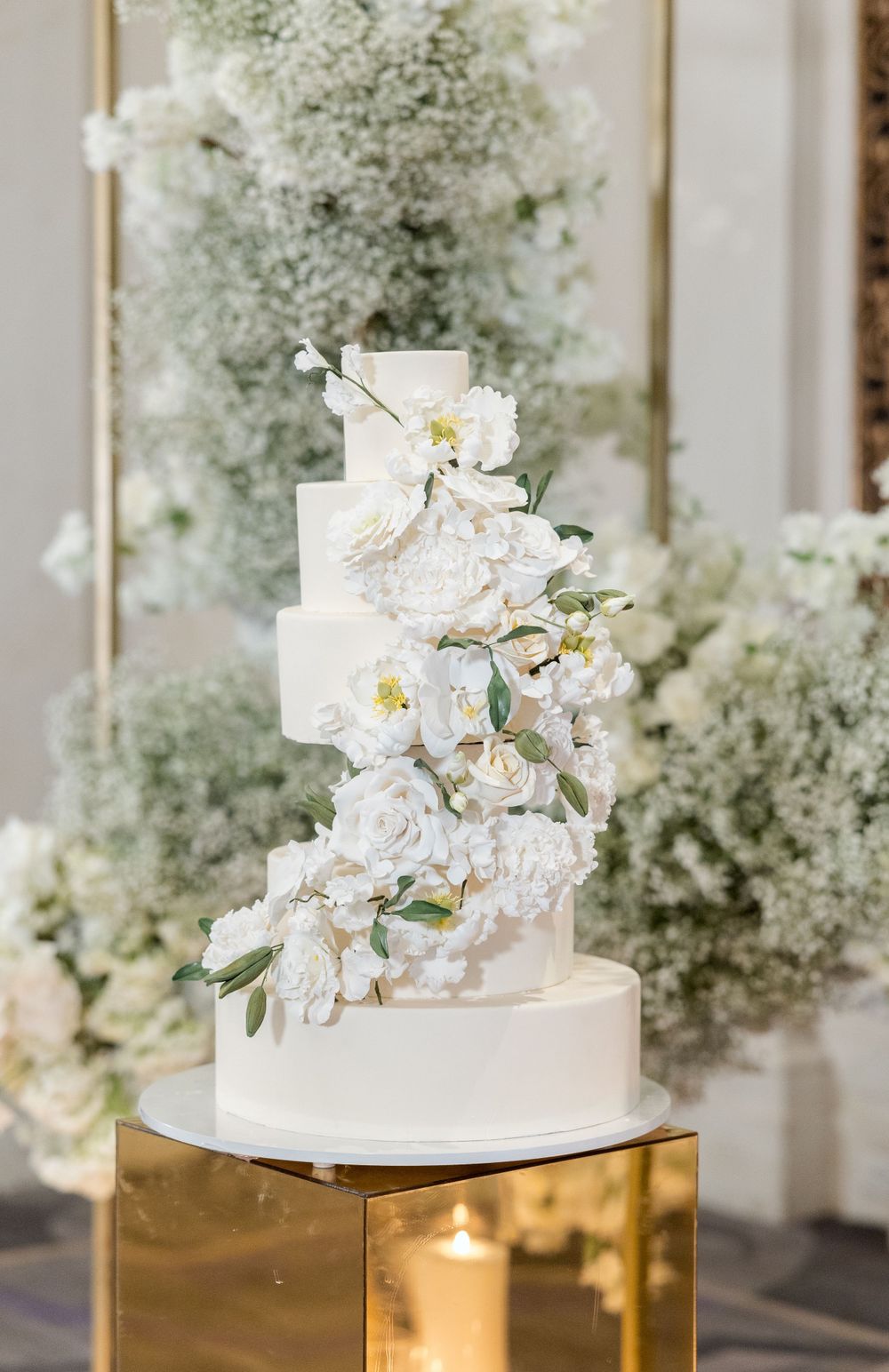 Elegant white wedding cake decorated with cascading flowers on gold stand.
