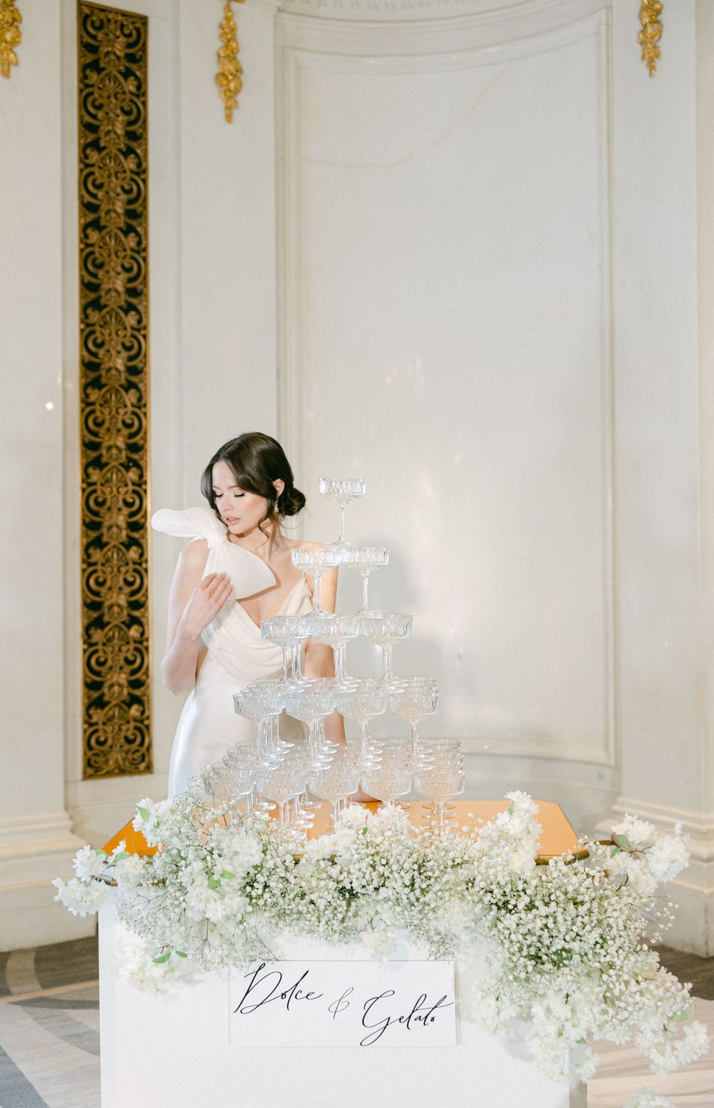 A champagne tower decorated with baby's breath flowers sits on an elegant wedding display.