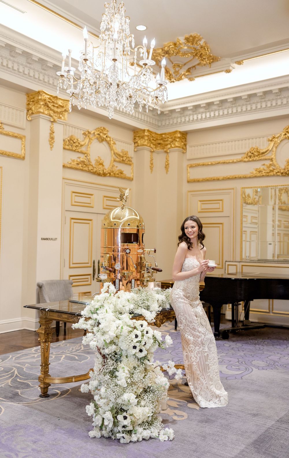 Luxurious ballroom with gold ornate details, crystal chandelier, and white floral arrangement.
