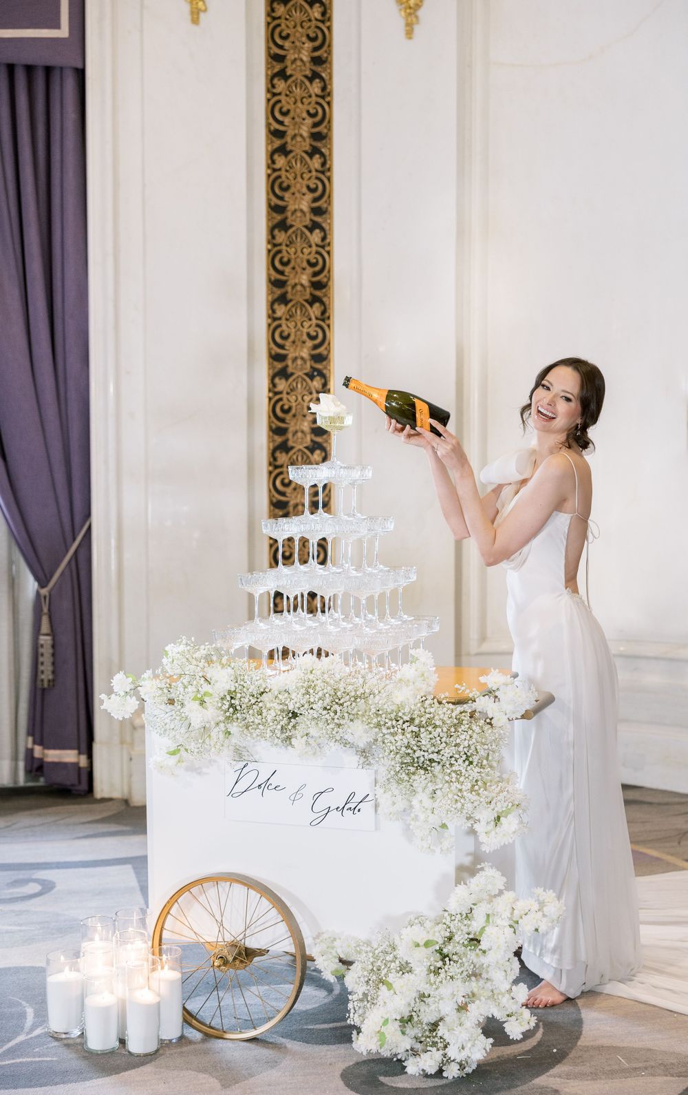 Elegant champagne tower setup with white floral decorations and candlelight at wedding reception.