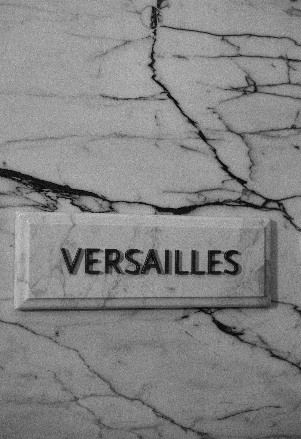 A marble wall with cracks features a sign reading 'VERSAILLES' in black text.