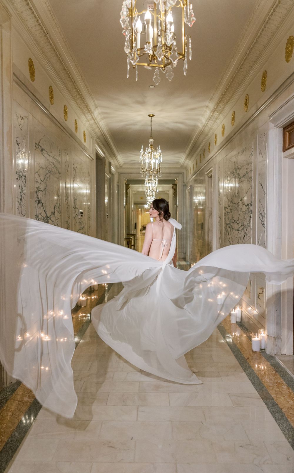 Flowing white gown twirling in ornate hallway with crystal chandeliers and candlelight.