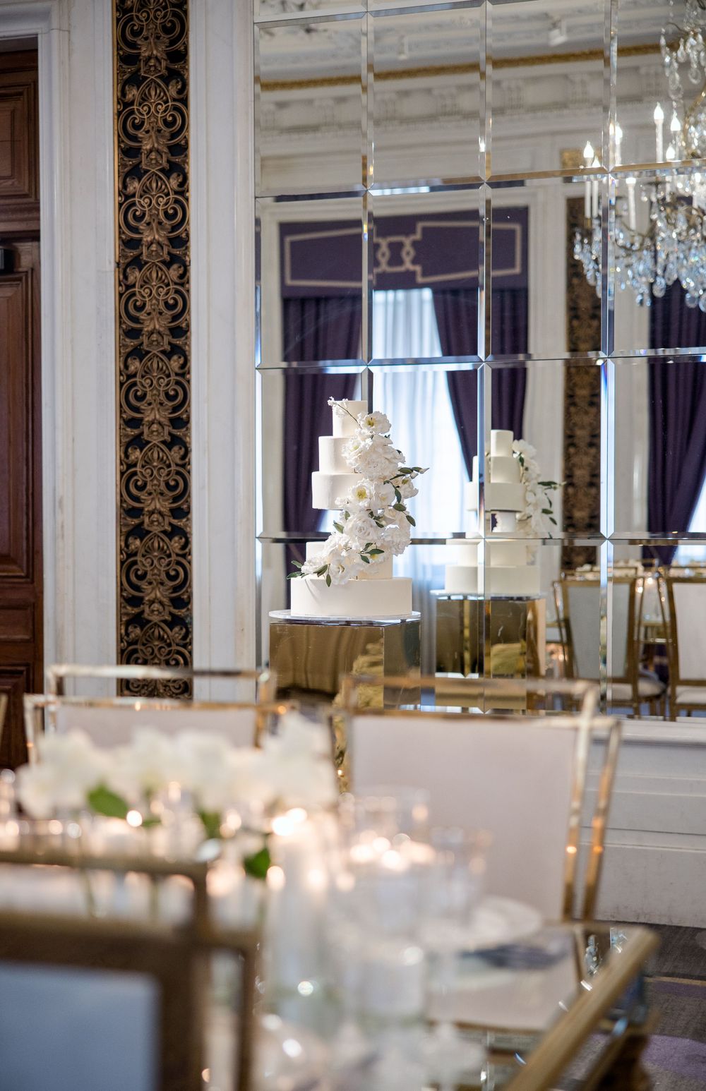 Luxurious wedding reception venue with ornate mirrors, crystal chandeliers, and tiered white wedding cake.