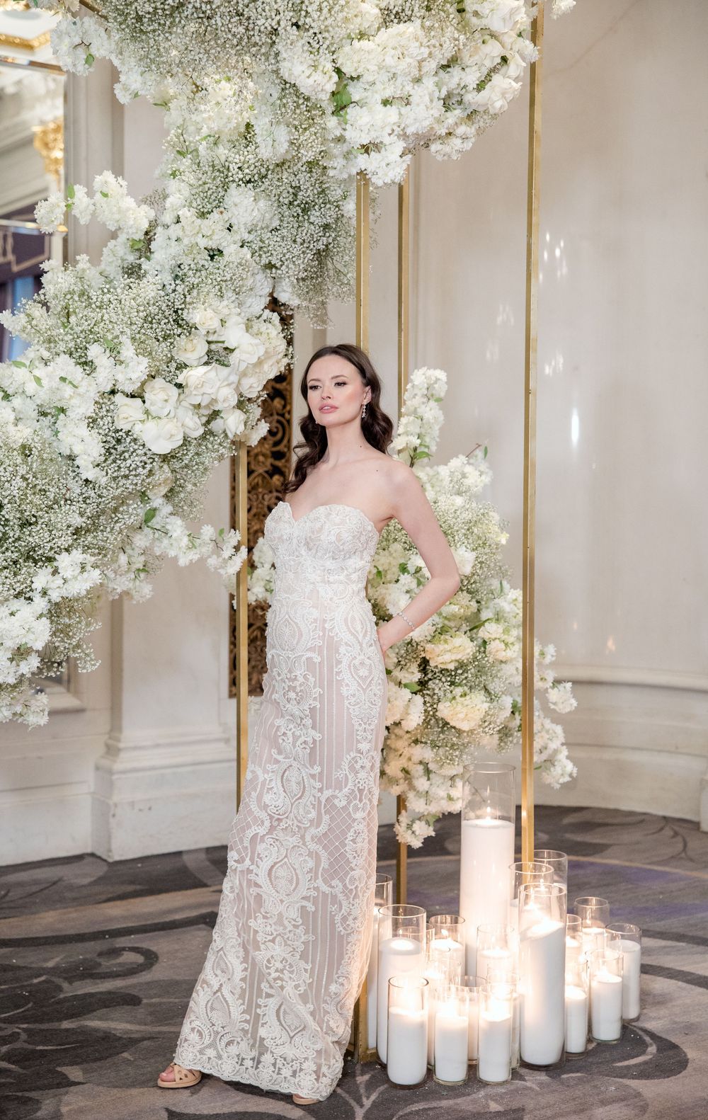 White floral installation with cascading blooms and glowing candles in luxurious venue.