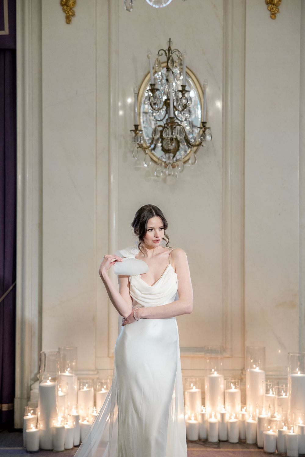 Romantic bridal portrait with candlelit backdrop and crystal chandelier in elegant setting.
