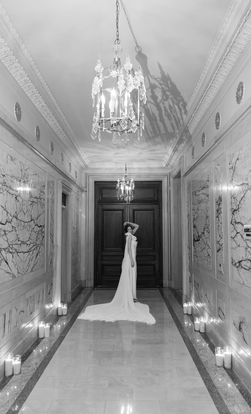 Long hallway with crystal chandeliers and candles featuring silhouette of bride in flowing gown.