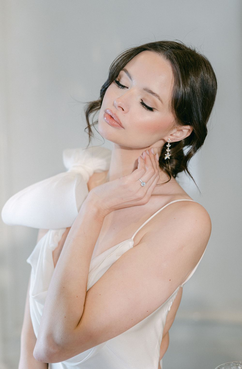 Romantic portrait of bride in soft white dress with eyes closed.