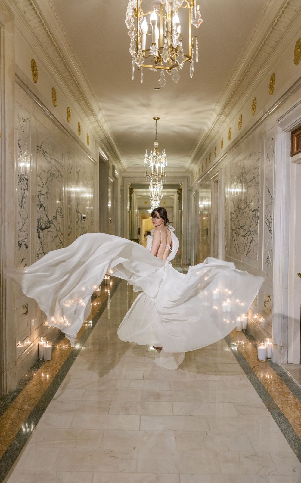 Wedding dress movement captured in elegant hallway with ornate wall details and chandeliers.