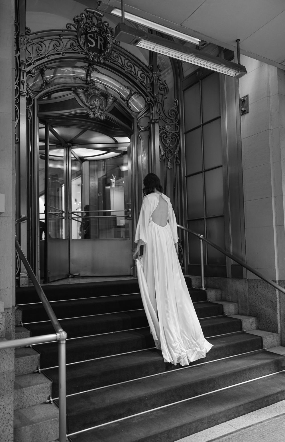 A person in a white dress ascends ornate stairs through an elaborate archway.