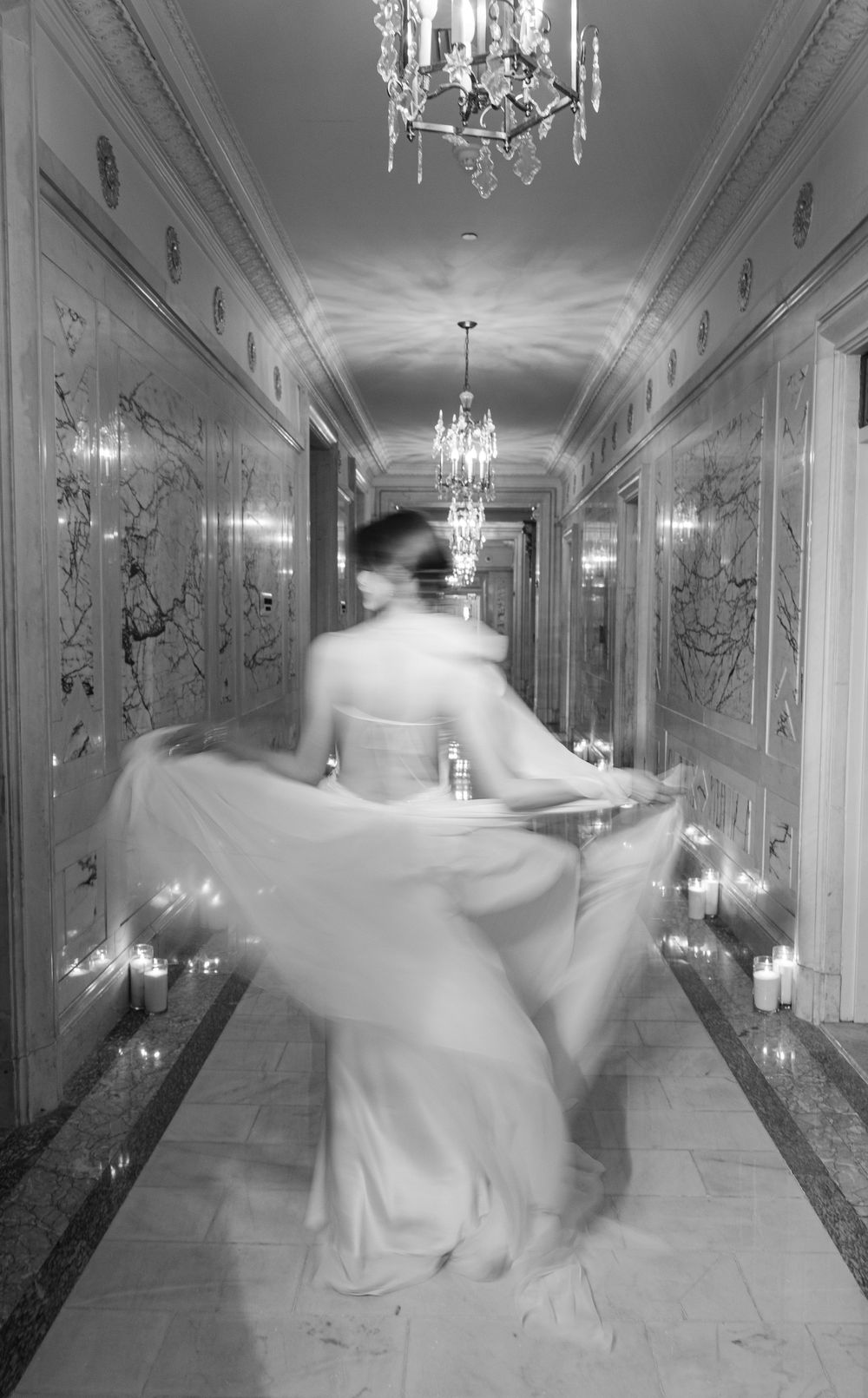 Motion-blur black and white photo of spinning wedding dress in candlelit corridor.