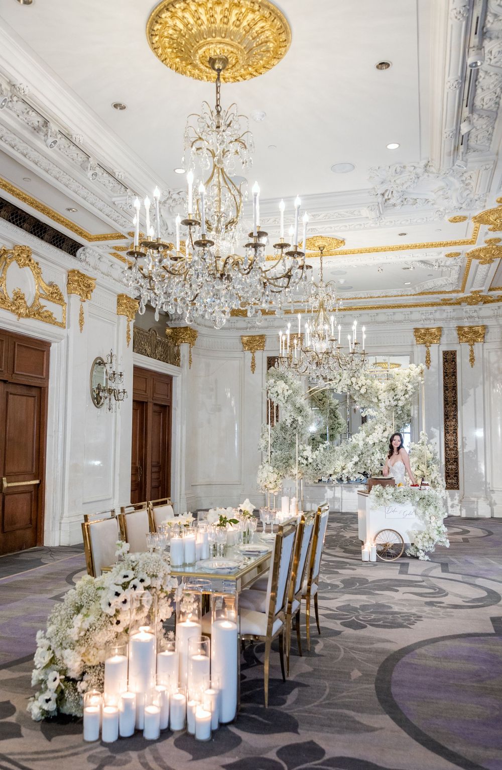 Luxurious wedding reception room with crystal chandeliers, floral arrangements and candle-lit table setting.