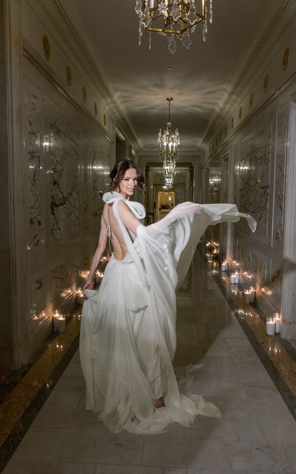 Ethereal bridal portrait in backlit hallway with floating dress and candlelight.