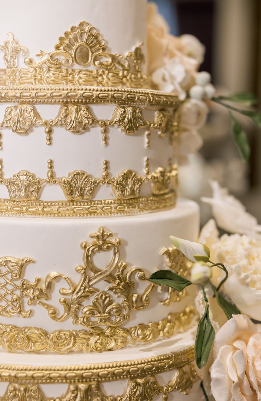 Wedding cake with intricate gold crown details and delicate peach roses.