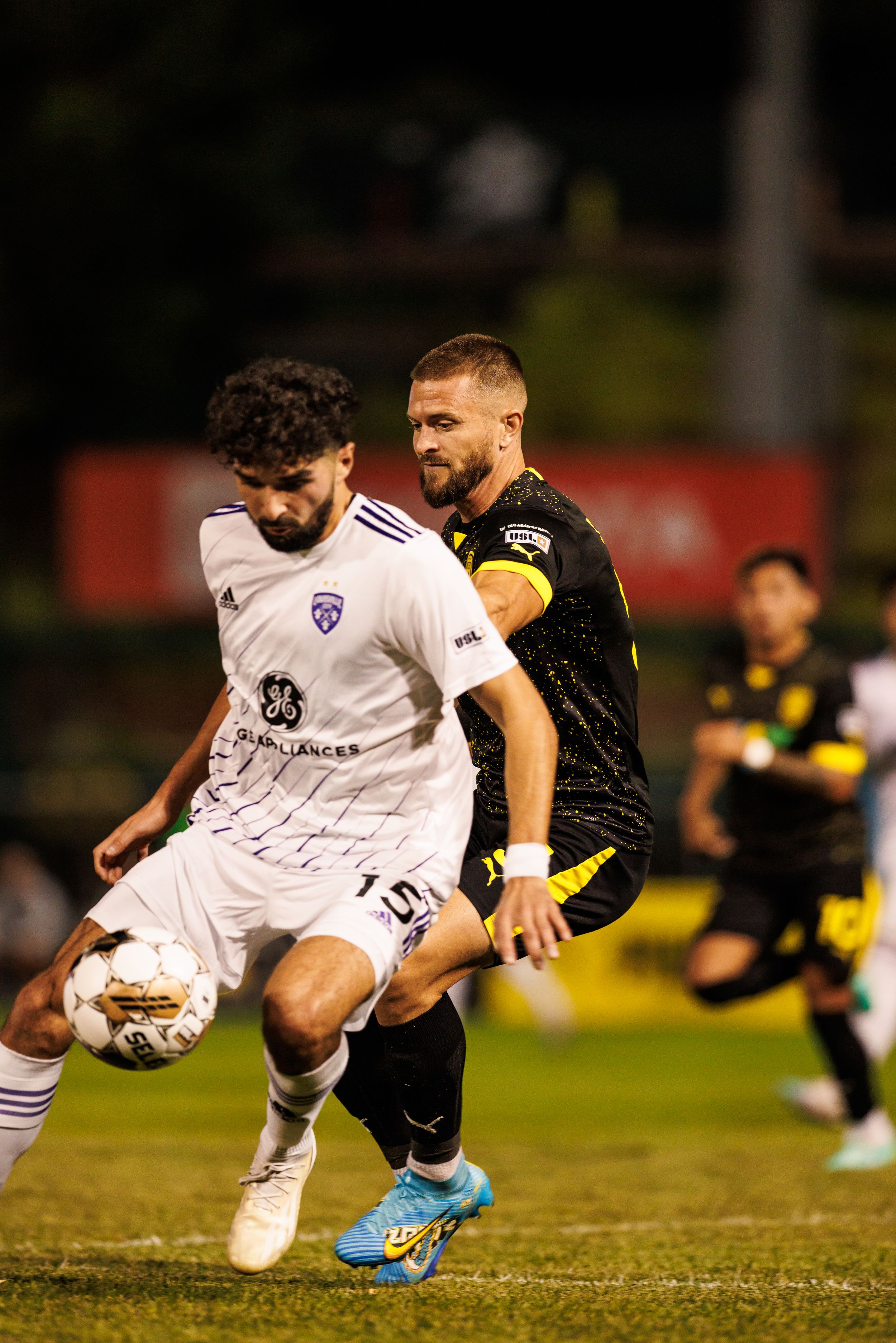 Soccer players from opposing teams battle for possession of the ball during night match.