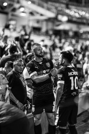 Soccer team members interact with fans near sideline during black and white nighttime shot.