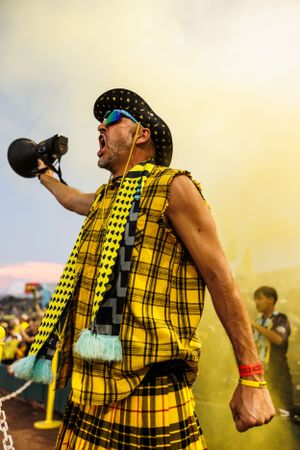 Fan in bright yellow plaid outfit cheers with microphone at sporting event.