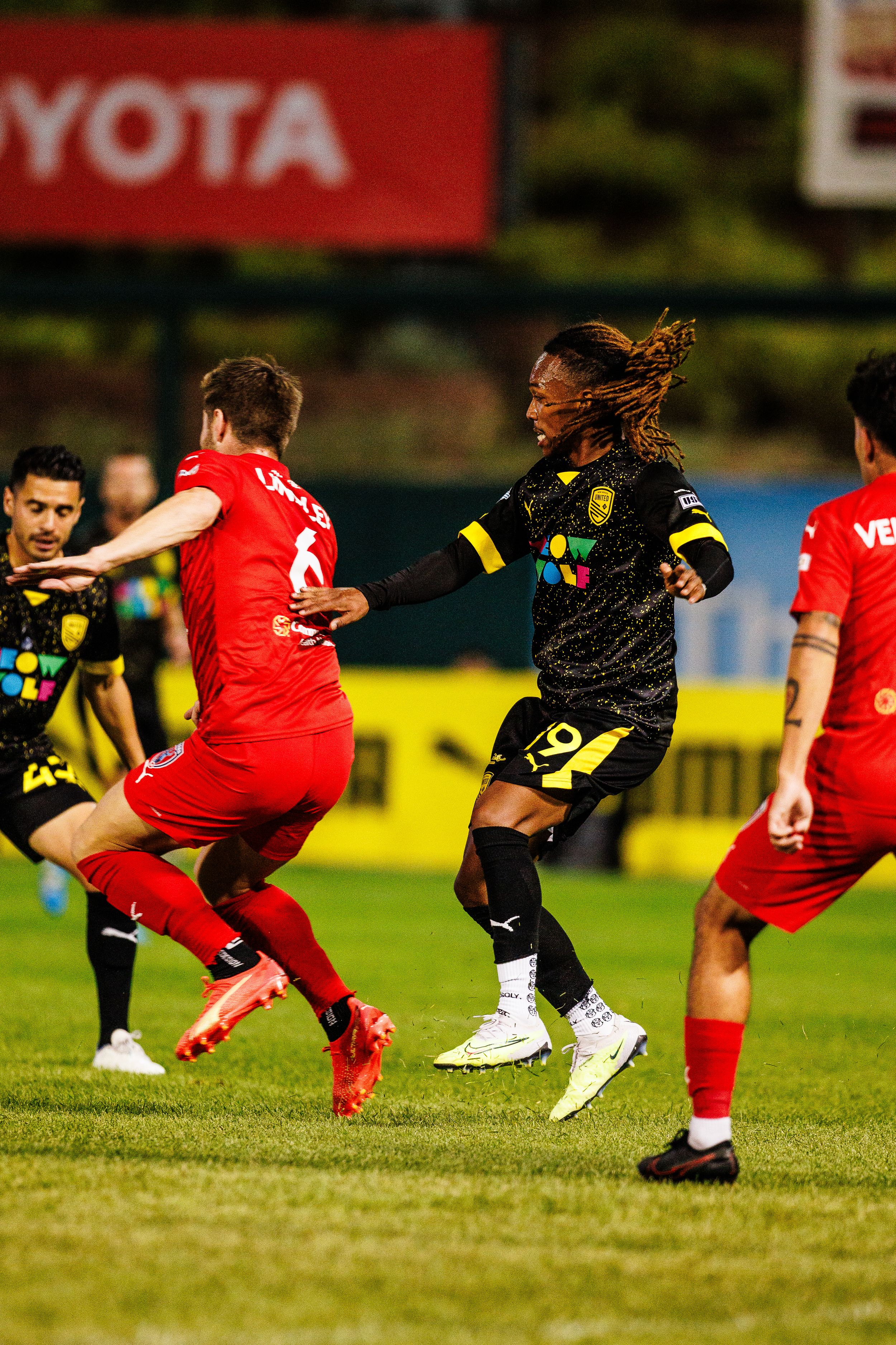 Soccer players in red and black uniforms battle for possession during competitive match.