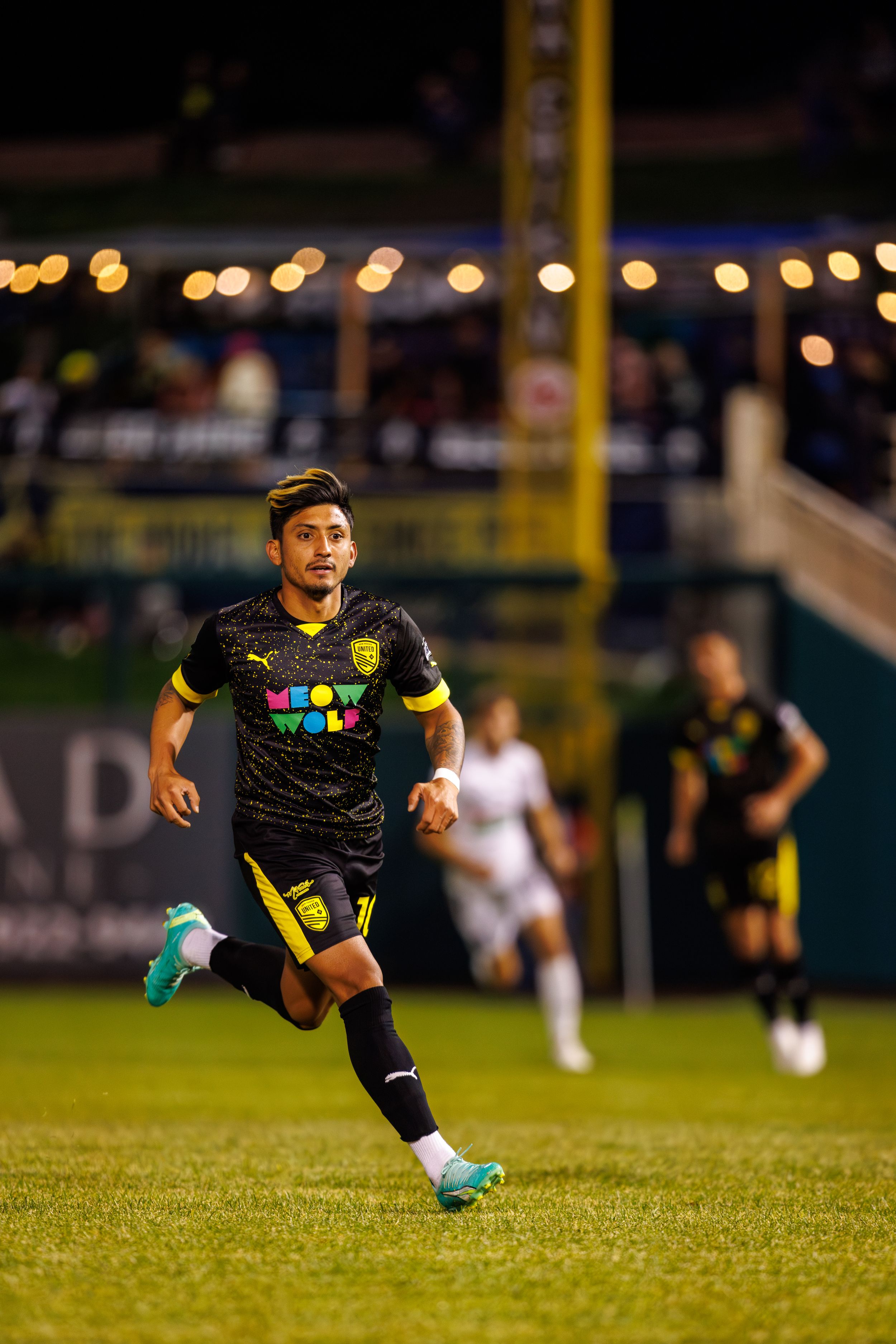 Soccer player in black and yellow jersey sprints across field at night.