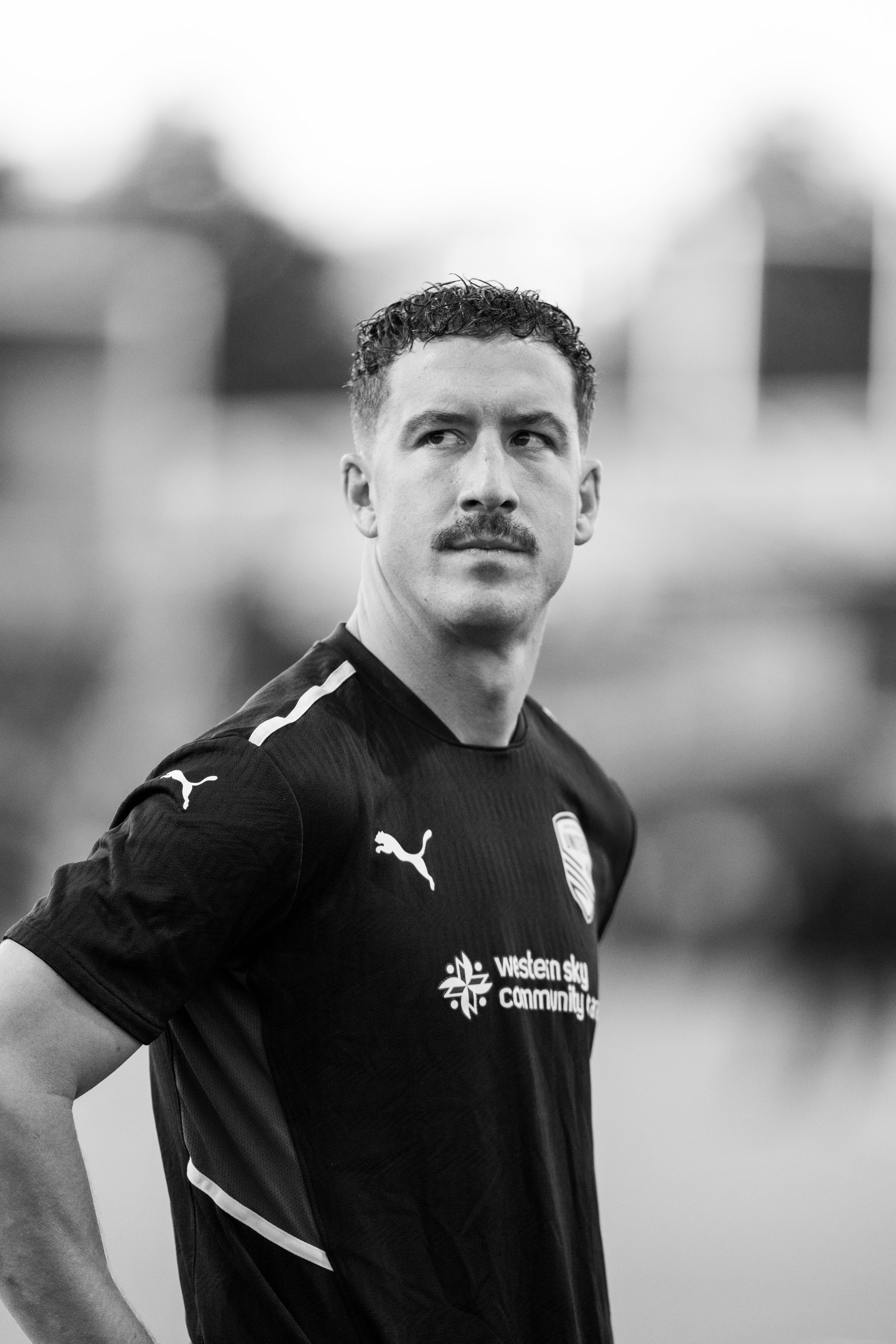Soccer player in black Puma jersey poses for portrait against blurred background.