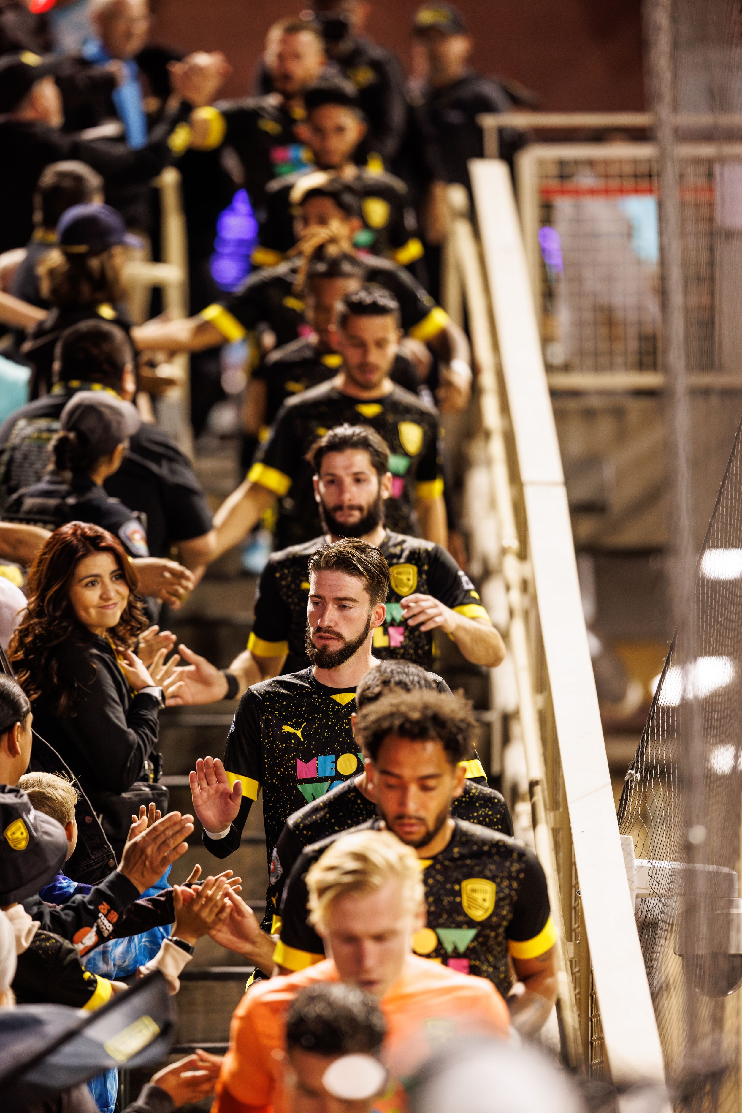 Soccer team interacting with fans along stadium walkway.