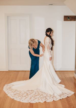 Wedding dress being arranged to show off intricate lace train on hardwood floor.
