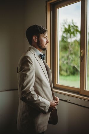 Person in light colored suit gazes thoughtfully out windows.