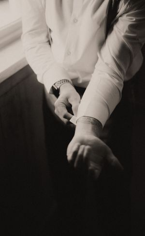 A close-up black and white photo showing hands and formal attire details at a wedding.