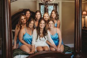 Bridal party in blue dresses lounges on bed during wedding preparations.